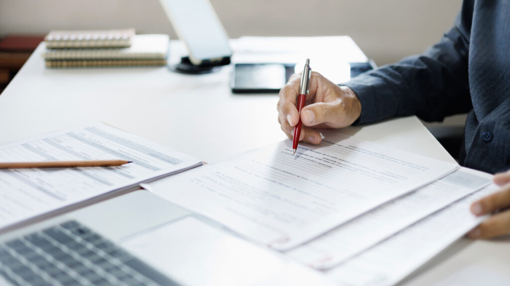 A man in a blazer holds a pen as he reads through a new form to be filled out